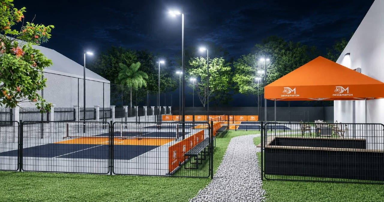 Outdoor courts at night beside a lawn path, with an orange Dink&Match canopy over courtside seating