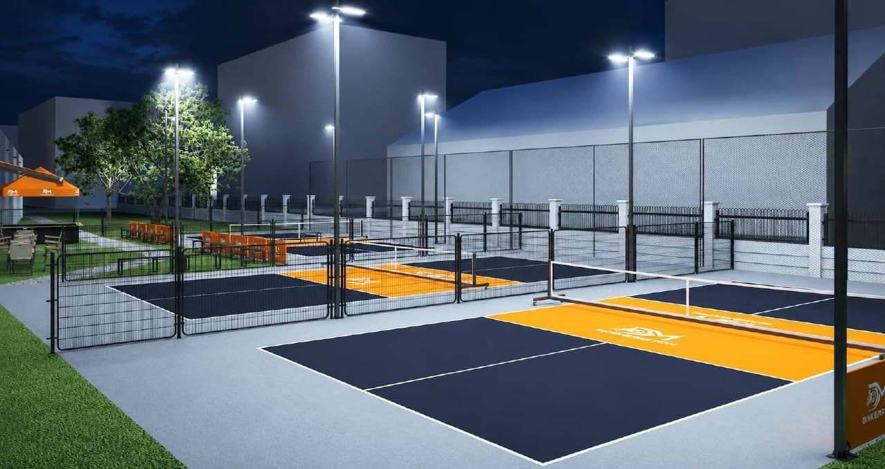 Floodlit outdoor courts at night seen from the walkway, with trees and the clubhouse behind